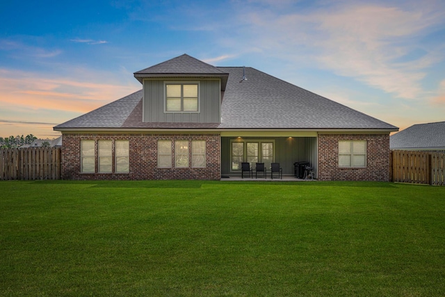 back of house at dusk with a patio, a lawn, brick siding, and a fenced backyard