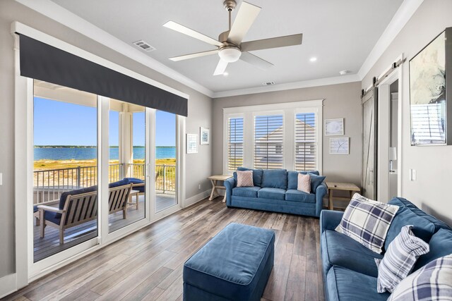 living room with wood-type flooring, a wealth of natural light, a barn door, ceiling fan, and a water view