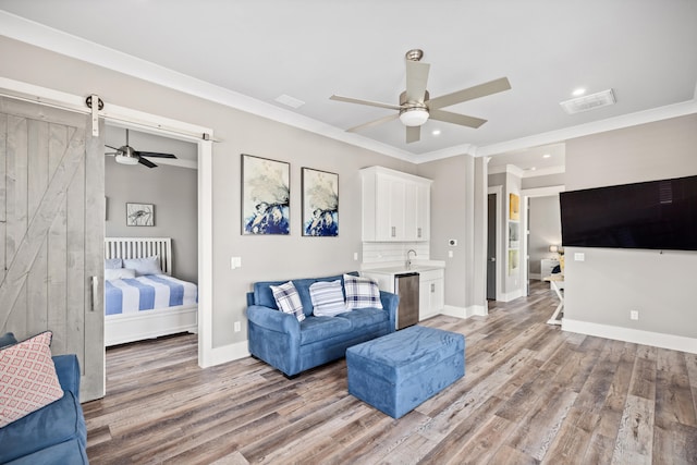 interior space with ensuite bathroom, a barn door, wood-type flooring, ceiling fan, and ornamental molding