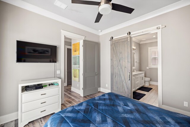 bedroom featuring ornamental molding, ensuite bath, ceiling fan, hardwood / wood-style flooring, and a barn door