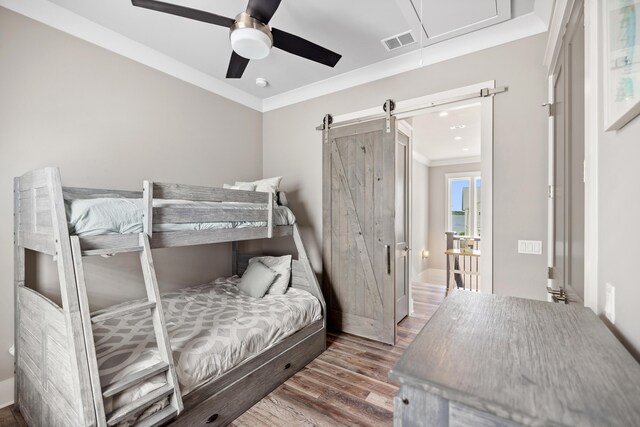 bedroom featuring crown molding, wood-type flooring, ceiling fan, and a barn door