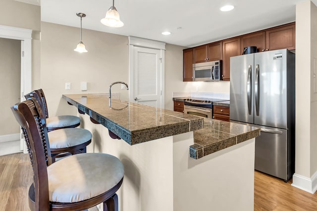 kitchen featuring a kitchen breakfast bar, pendant lighting, appliances with stainless steel finishes, kitchen peninsula, and light wood-type flooring