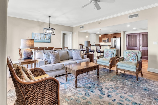 living room featuring ceiling fan with notable chandelier, light hardwood / wood-style floors, and crown molding