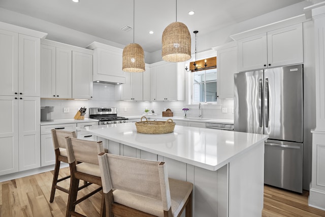 kitchen with appliances with stainless steel finishes, white cabinets, light hardwood / wood-style floors, and a kitchen island