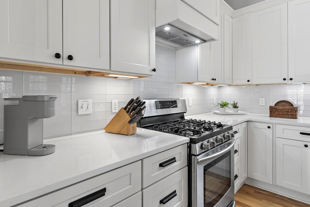 kitchen with backsplash, white cabinetry, gas range, light hardwood / wood-style flooring, and custom range hood