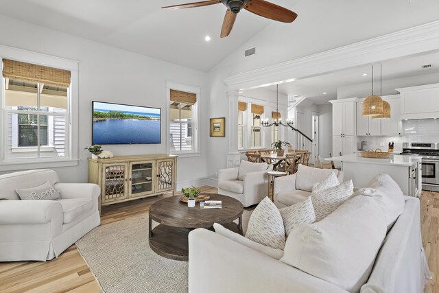 living room with lofted ceiling, light hardwood / wood-style flooring, ceiling fan with notable chandelier, and a healthy amount of sunlight