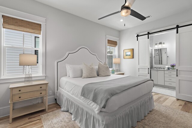 bedroom featuring connected bathroom, ceiling fan, light hardwood / wood-style flooring, and a barn door