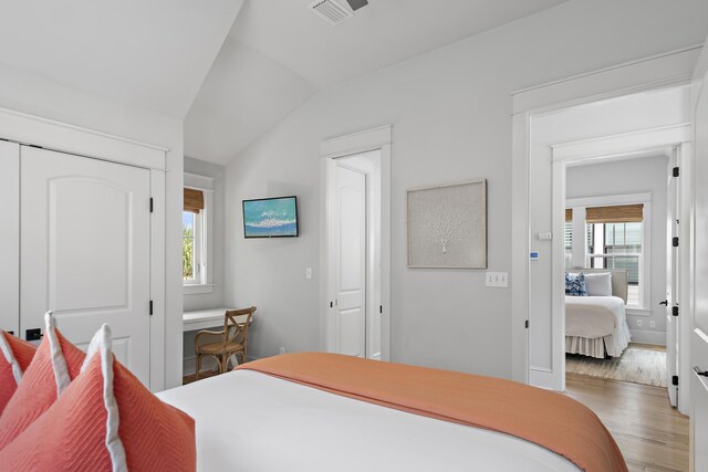 bedroom with lofted ceiling, multiple windows, a closet, and hardwood / wood-style floors