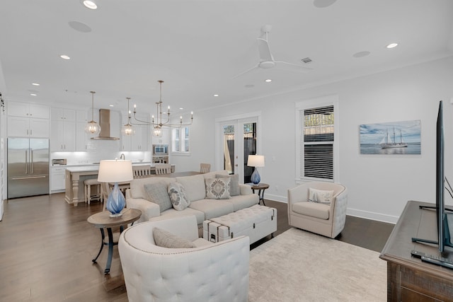 living room with ceiling fan with notable chandelier, ornamental molding, and wood-type flooring