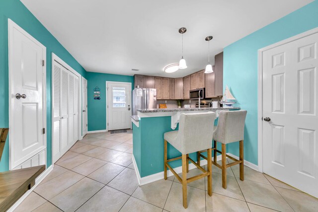 kitchen with light tile patterned floors, stainless steel appliances, a kitchen breakfast bar, kitchen peninsula, and pendant lighting