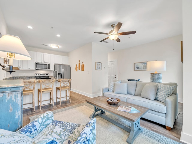 living room with light wood finished floors, recessed lighting, a ceiling fan, and baseboards