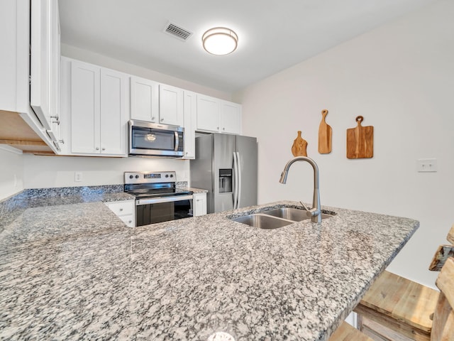 kitchen featuring visible vents, light stone counters, white cabinets, stainless steel appliances, and a sink