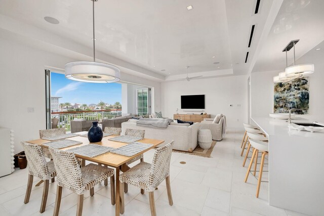 tiled dining room with ceiling fan, a raised ceiling, and sink