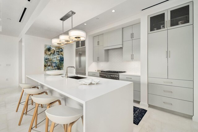 kitchen featuring decorative backsplash, stainless steel stove, a kitchen bar, a center island with sink, and sink