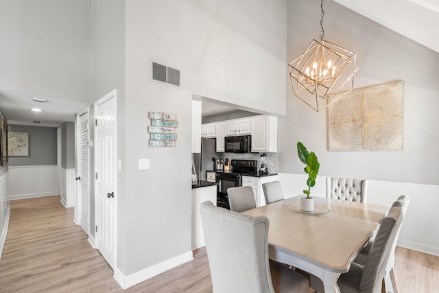 dining area with light wood-type flooring, an inviting chandelier, and a high ceiling