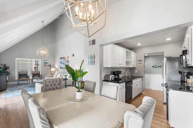 dining area featuring an inviting chandelier, light wood-type flooring, sink, high vaulted ceiling, and beam ceiling