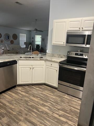 kitchen with light wood-type flooring, sink, light stone countertops, ceiling fan, and appliances with stainless steel finishes