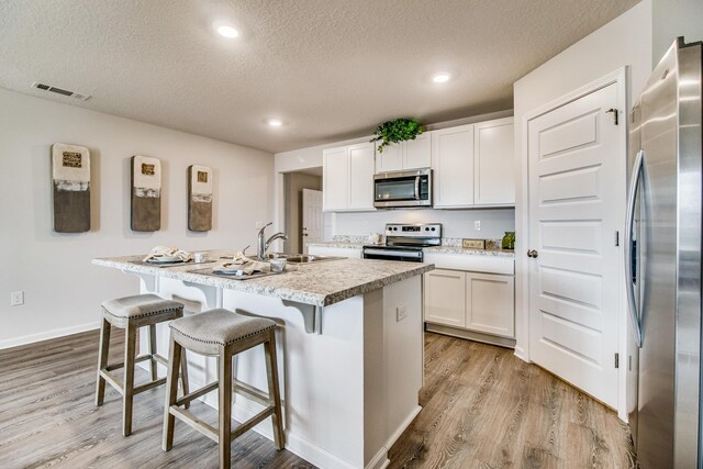 6324 Firefly Dr, Milton, FL 32583 - kitchen with appliances with stainless steel finishes, light wood-style floors, a textured ceiling, an island with sink, and a sink