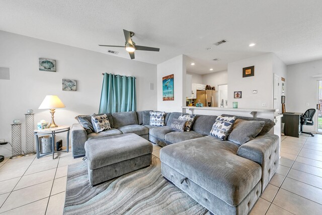 living room featuring ceiling fan, light tile patterned flooring, and a textured ceiling