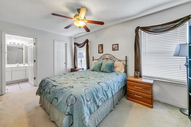 bedroom with ceiling fan, light colored carpet, a textured ceiling, and ensuite bathroom