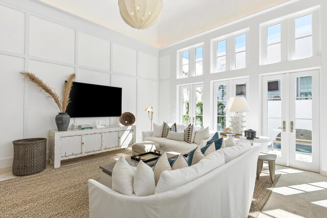 carpeted living room featuring a notable chandelier, a towering ceiling, plenty of natural light, and french doors