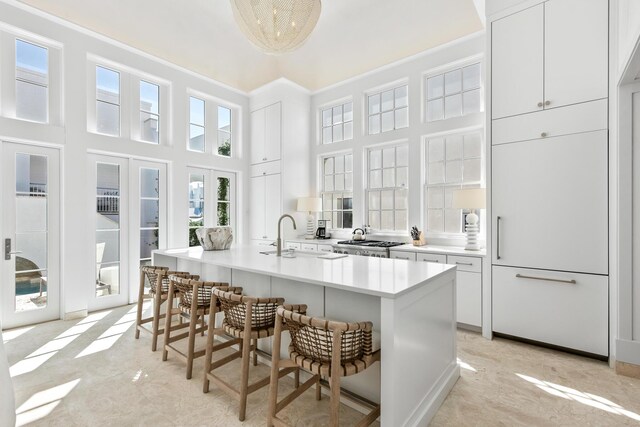 kitchen featuring a kitchen breakfast bar, a towering ceiling, an island with sink, white cabinets, and sink