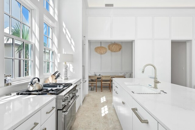 kitchen with high end stove, a wealth of natural light, sink, and white cabinets