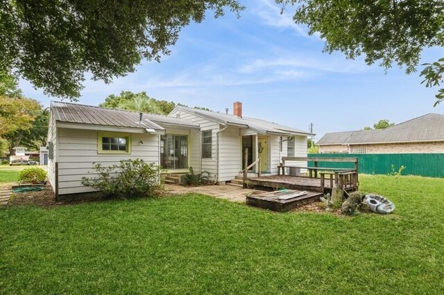 back of property with a deck, fence, a yard, metal roof, and a chimney