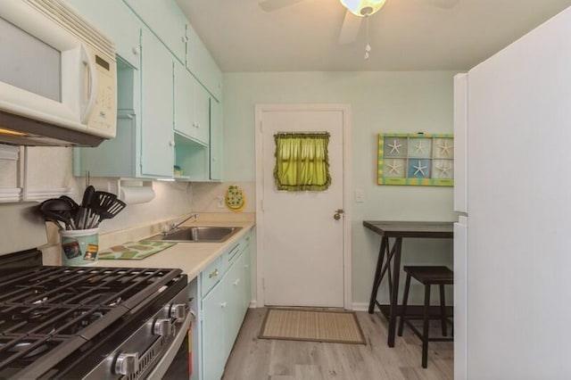 kitchen with a sink, light countertops, white microwave, ceiling fan, and stainless steel gas range