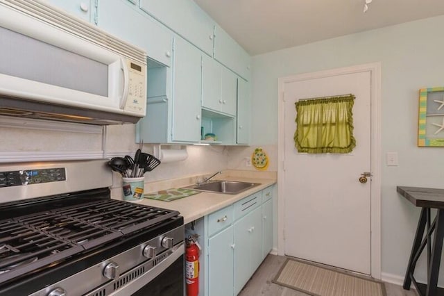 kitchen featuring white microwave, blue cabinetry, stainless steel range with gas cooktop, and a sink