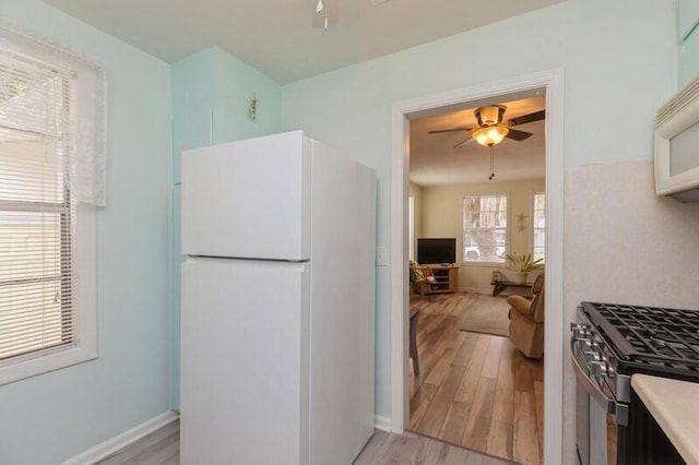 kitchen featuring light wood-type flooring, white appliances, baseboards, and a ceiling fan