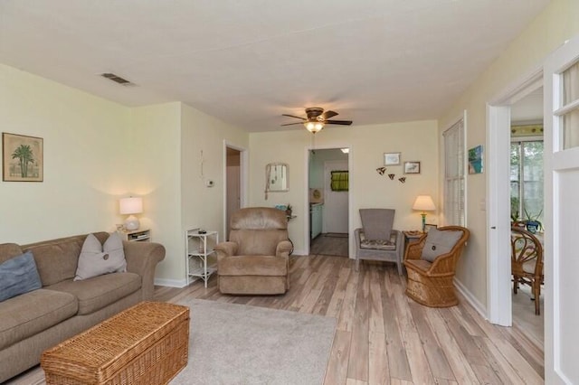 living room featuring light wood finished floors, visible vents, baseboards, and a ceiling fan