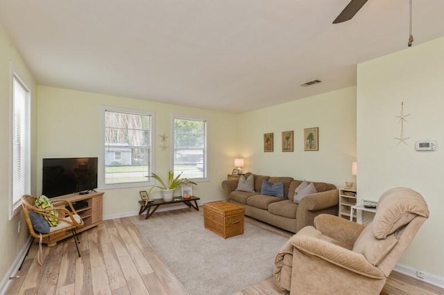 living room featuring light wood-type flooring, visible vents, baseboards, and a ceiling fan