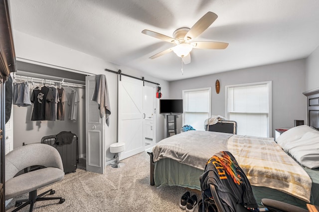 bedroom with a textured ceiling, ceiling fan, a closet, a barn door, and carpet floors