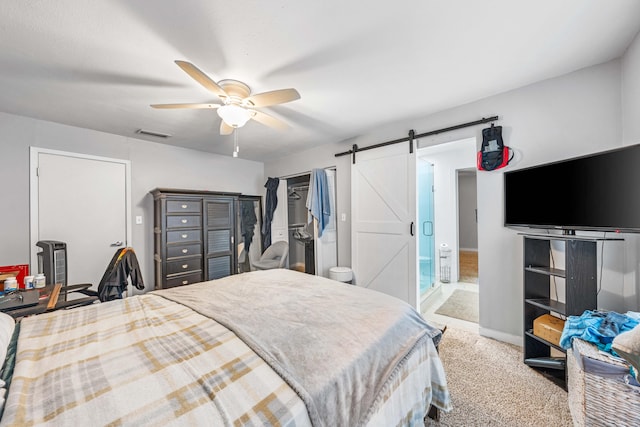 carpeted bedroom with a barn door, ceiling fan, and ensuite bathroom