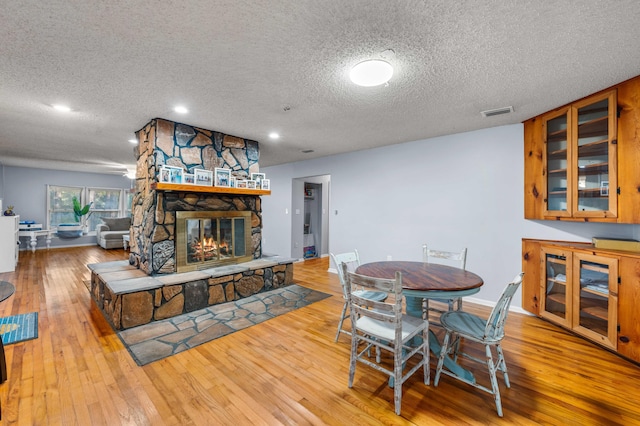 dining space with light hardwood / wood-style flooring, a textured ceiling, and a stone fireplace