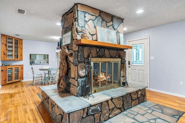 living room with a textured ceiling, a stone fireplace, and light wood-type flooring