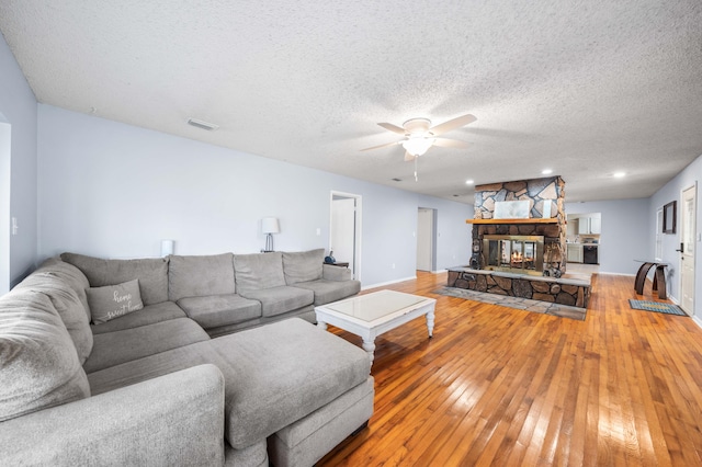 living room with a textured ceiling, hardwood / wood-style floors, ceiling fan, and a stone fireplace