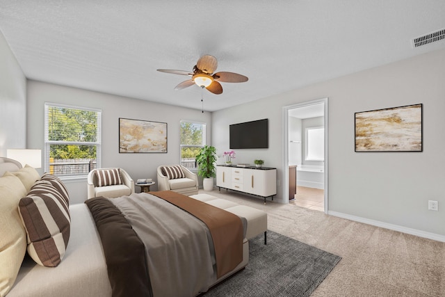 bedroom with ceiling fan, a textured ceiling, light carpet, and ensuite bath