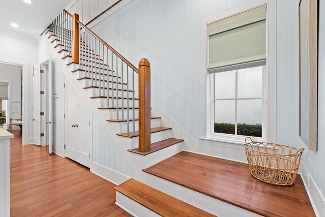 stairway with ornamental molding and wood-type flooring