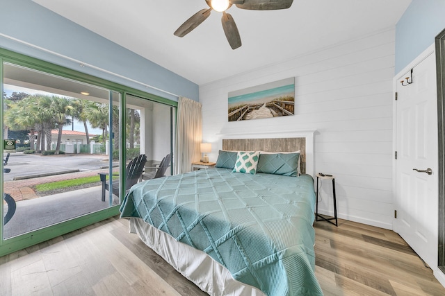 bedroom featuring ceiling fan, hardwood / wood-style flooring, wooden walls, and access to outside