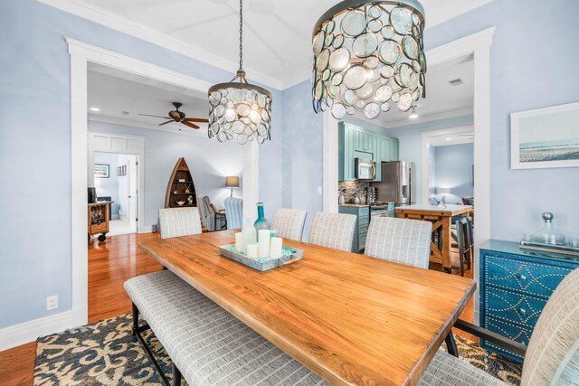 dining space featuring hardwood / wood-style flooring, ceiling fan with notable chandelier, and crown molding