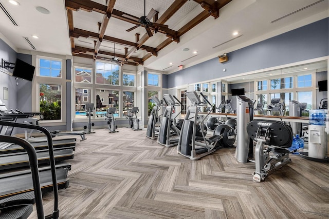 gym with ceiling fan, plenty of natural light, a towering ceiling, and coffered ceiling