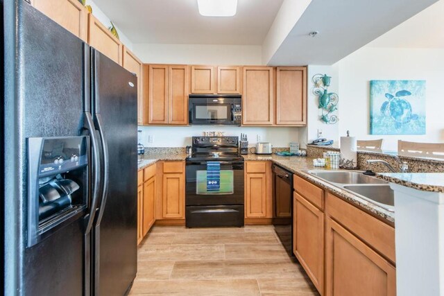 kitchen with light wood-type flooring, black appliances, light stone counters, kitchen peninsula, and sink