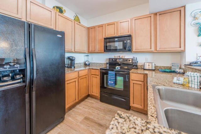 kitchen with light brown cabinetry, light stone countertops, light hardwood / wood-style floors, sink, and black appliances