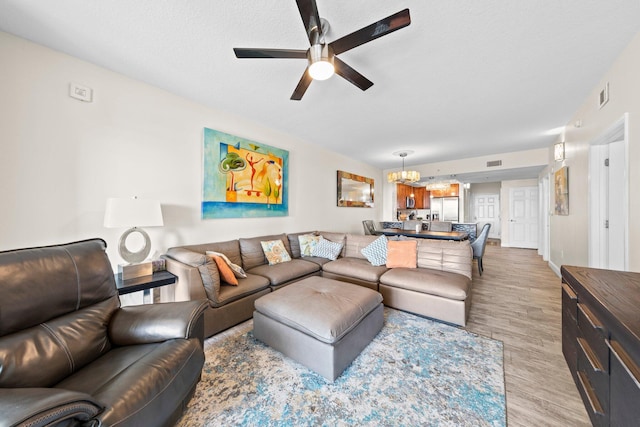 living room featuring ceiling fan with notable chandelier, light wood-type flooring, and a textured ceiling