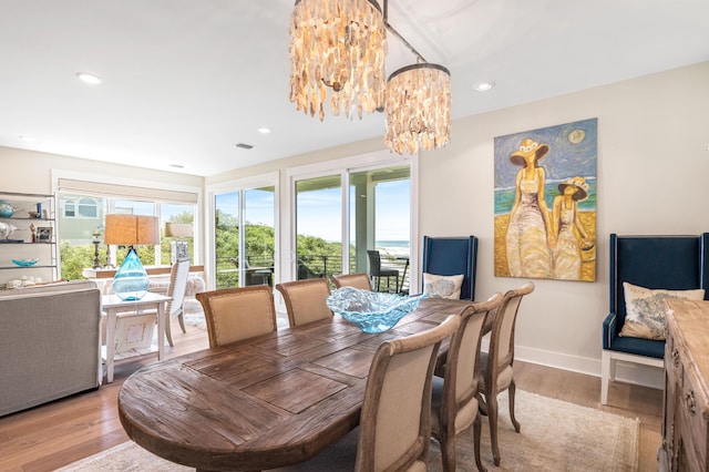 dining space with light wood finished floors, a notable chandelier, a healthy amount of sunlight, and baseboards