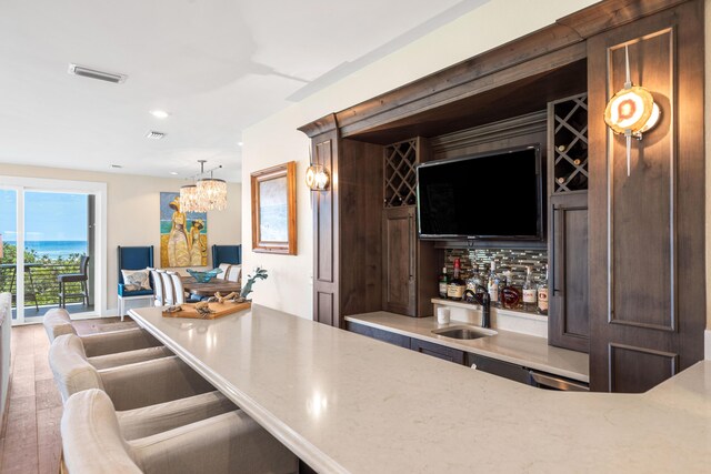 bar featuring light stone countertops, pendant lighting, a notable chandelier, hardwood / wood-style floors, and sink