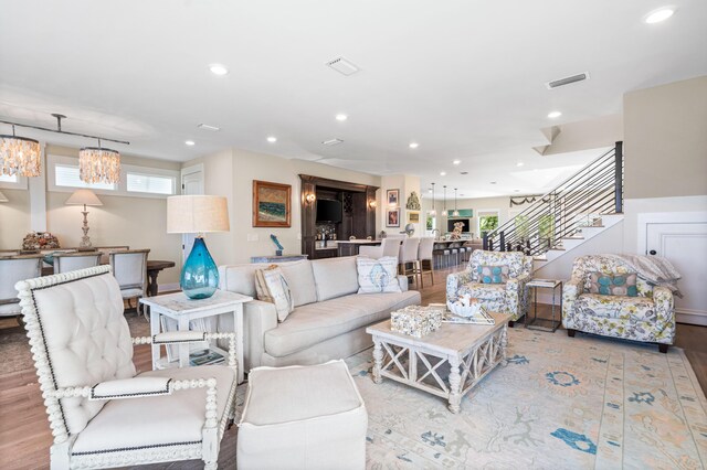living area featuring visible vents, wood finished floors, recessed lighting, an inviting chandelier, and stairs