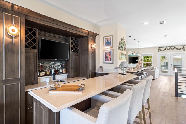 bar featuring hanging light fixtures, dark brown cabinetry, french doors, and light hardwood / wood-style floors